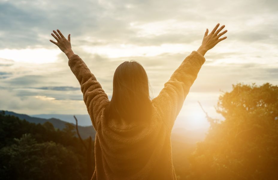 a female standing with her arms up in front of the sunrise
